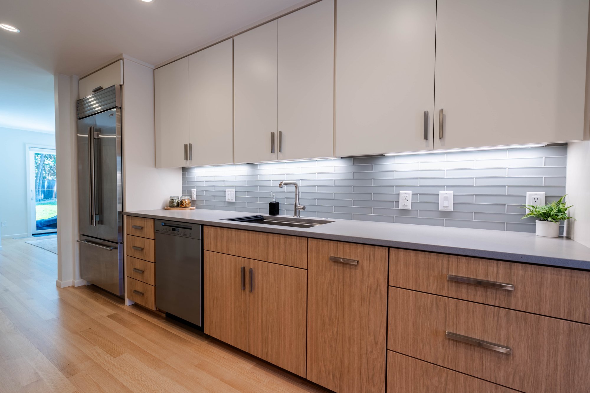 Modern kitchen with wood cabinetry, a large island with cooktop, stainless steel range hood, and light wood flooring.