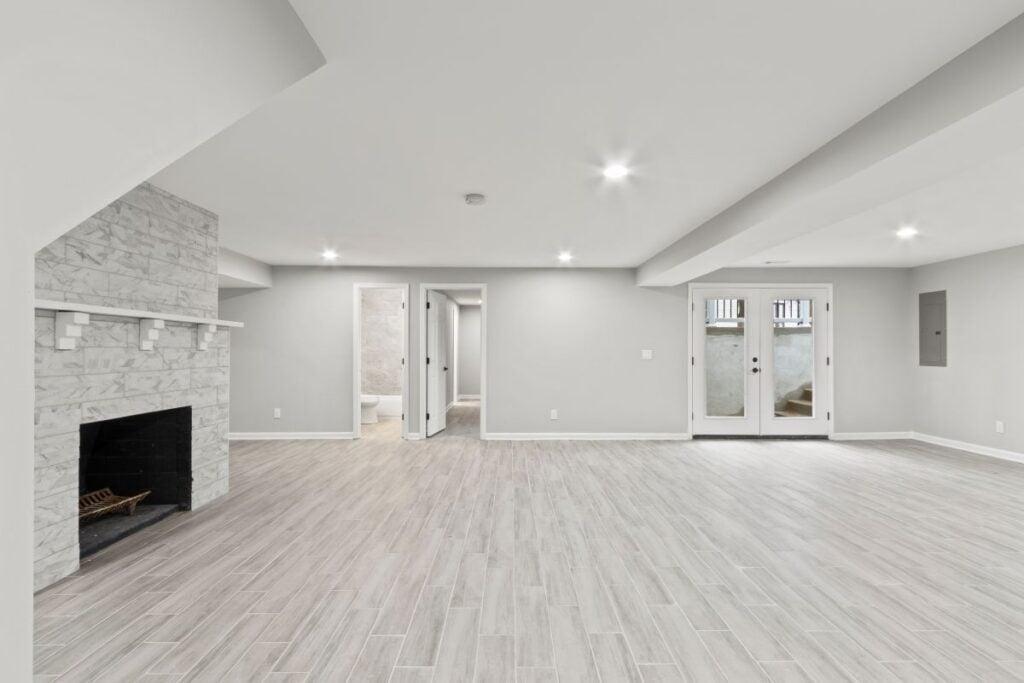 Modern finished basement featuring a stone fireplace, recessed lighting, and glass doors.