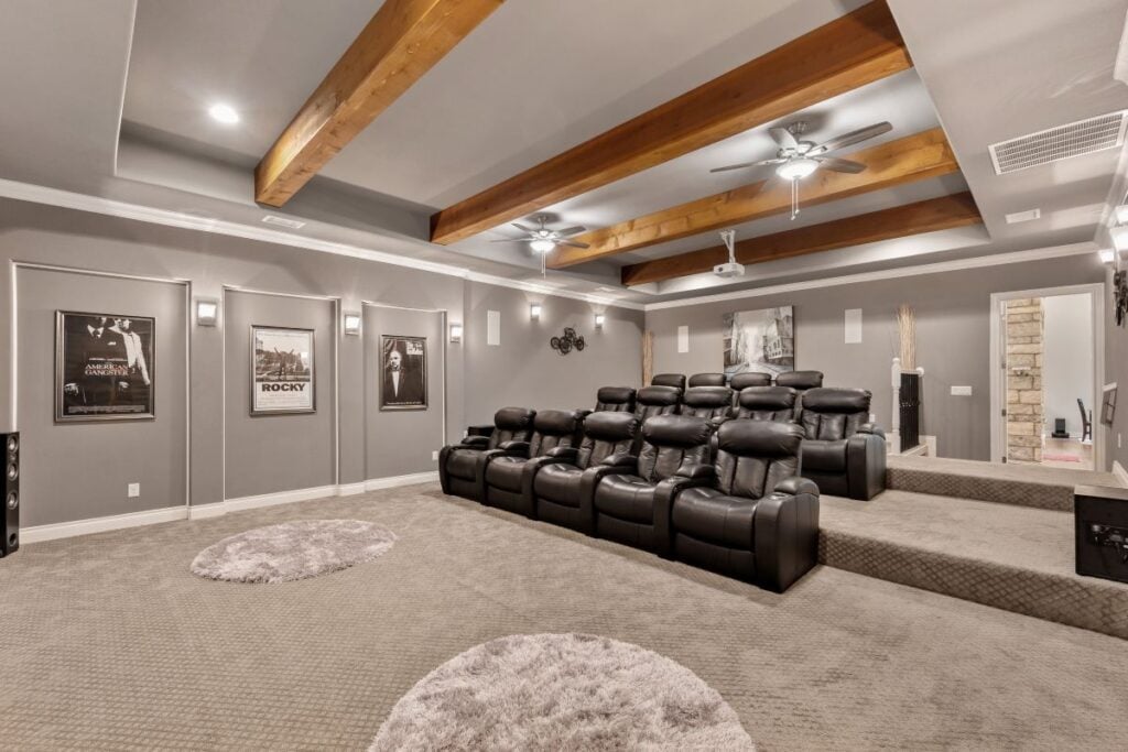 Finished basement theater room with wood beams, recessed lighting, and built-in platform flooring