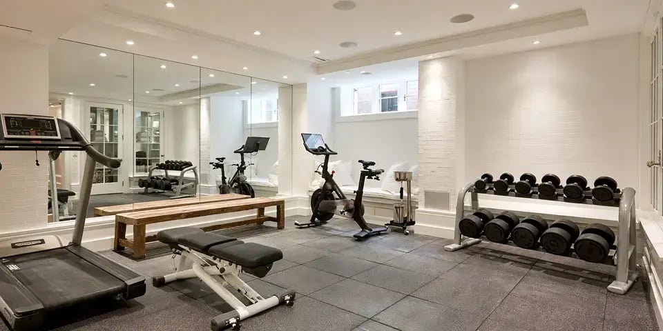 Finished basement home gym with treadmill, exercise bike, weight bench, dumbbell rack, and mirrored wall.