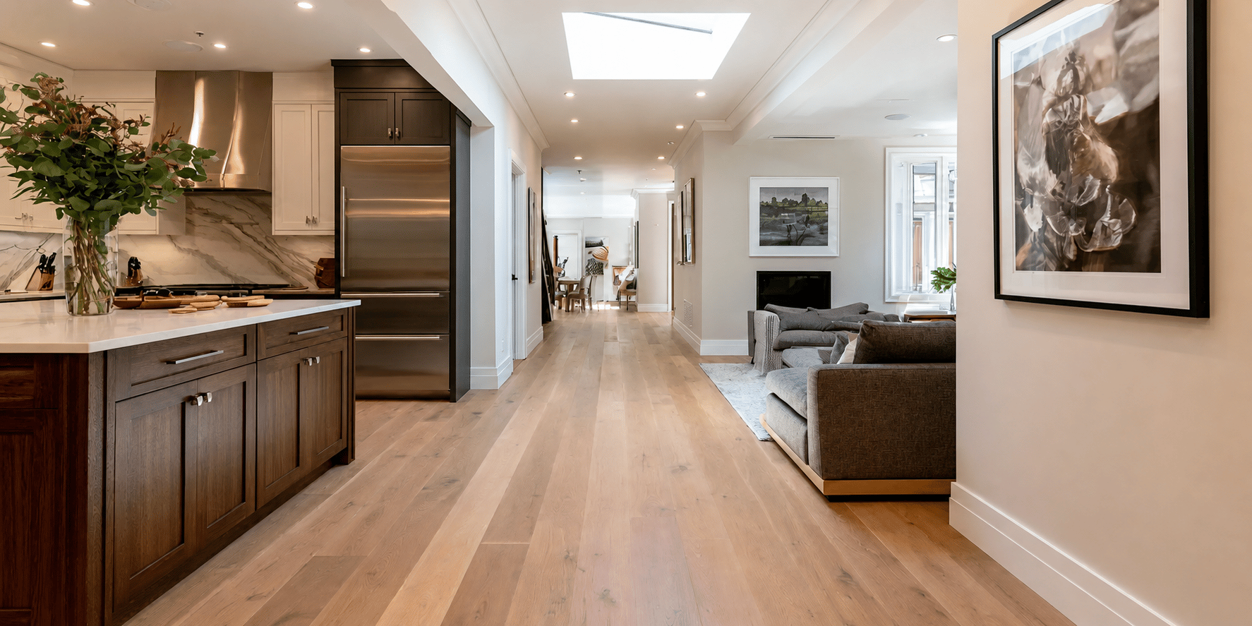 Open-concept remodeled interior with a custom kitchen, wide-plank wood flooring, skylight, and adjoining living area.