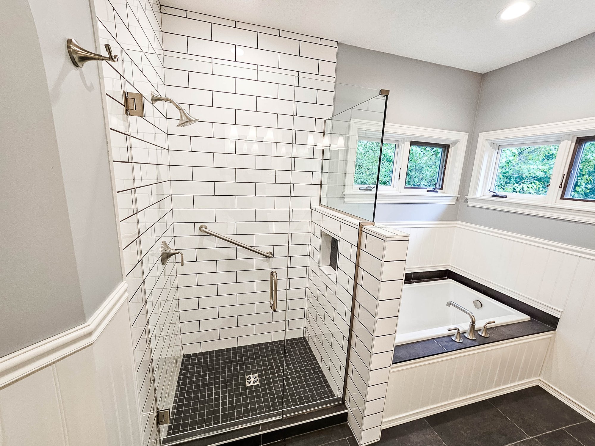 Bathroom remodeled by Homecare Remodeling featuring a white subway tile walk-in shower, glass enclosure, black tile flooring, and built-in bathtub.