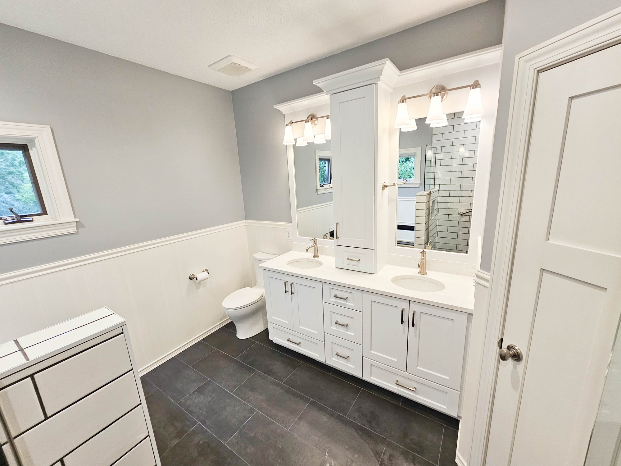 Bathroom remodeled by Homecare Remodeling featuring a white double vanity with a center storage cabinet, and dark tile flooring.