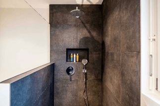 Walk-in shower with large dark wall tiles, rainfall showerhead, handheld sprayer, and recessed storage niche.