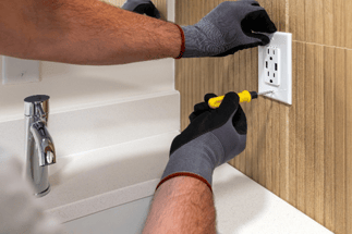 Electrician installing an electrical outlet beside a bathroom sink during a remodel.
