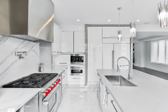 Modern white kitchen with a marble backsplash, large island sink, stainless steel range, and pendant lights.