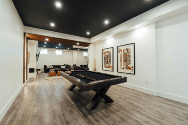Finished basement game room with a pool table, wood-look flooring, black ceiling, and lounge area.
