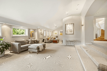 Bright finished basement with a patterned carpet, seating areas, and a staircase leading to the main level.