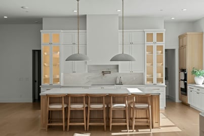 Modern kitchen remodel featuring white shaker cabinets, natural white oak island cabinetry, marble countertops and backsplash, glass-front cabinets, and oversized pendant lighting.