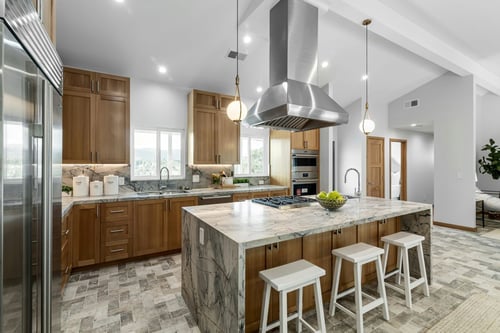 Modern kitchen with warm wood cabinetry, a marble waterfall island, stainless steel range hood, and white counter stools.