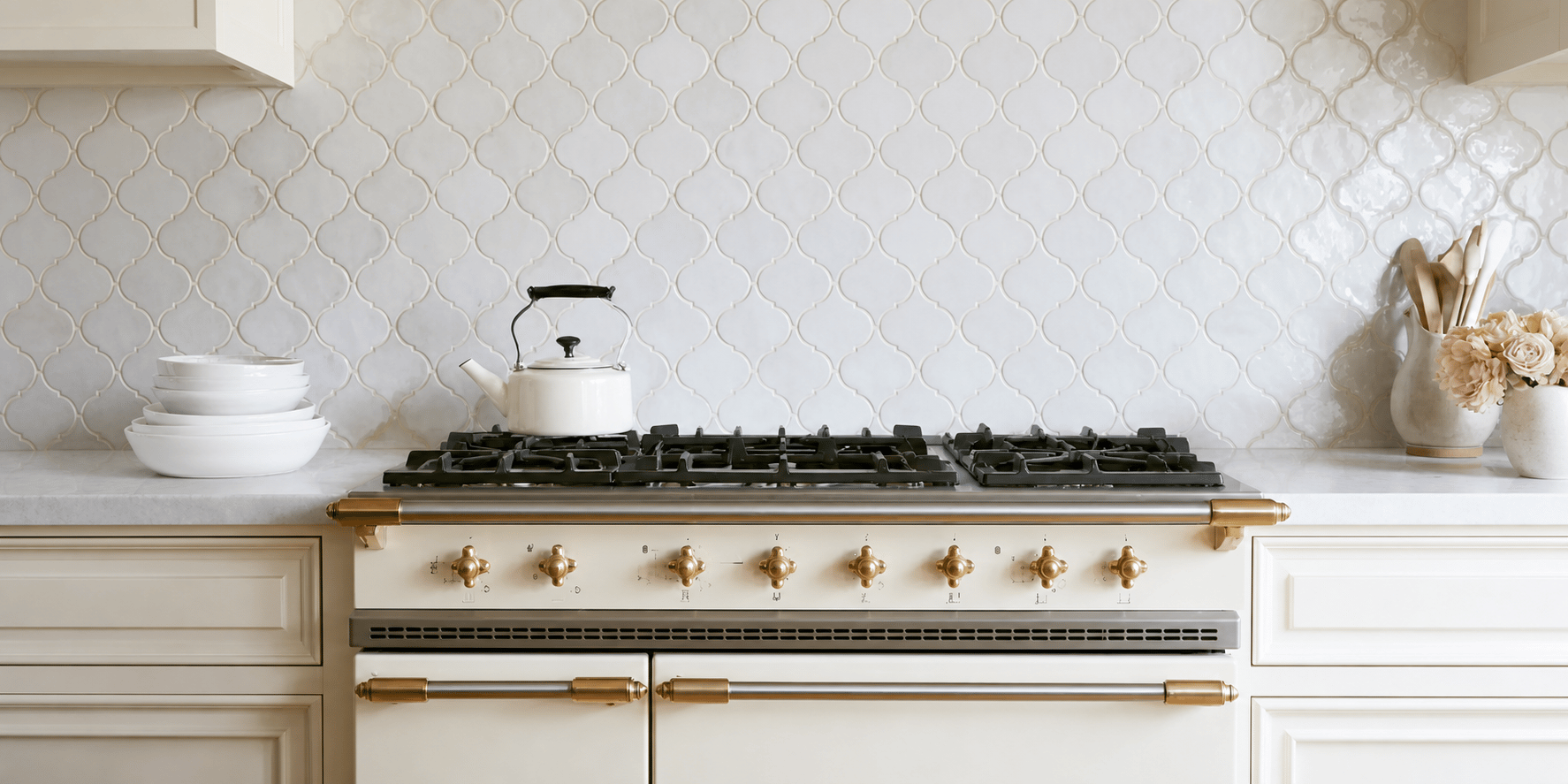 White kitchen range with brass hardware and a white patterned tile backsplash.