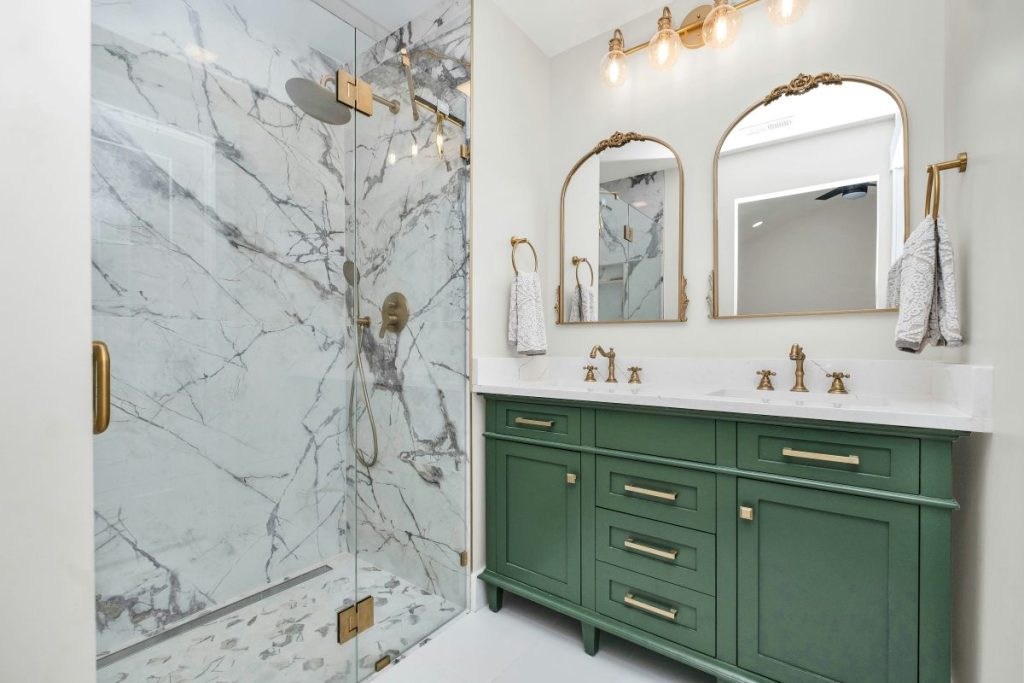 Remodeled bathroom with a green vanity, brass accents and a marble shower