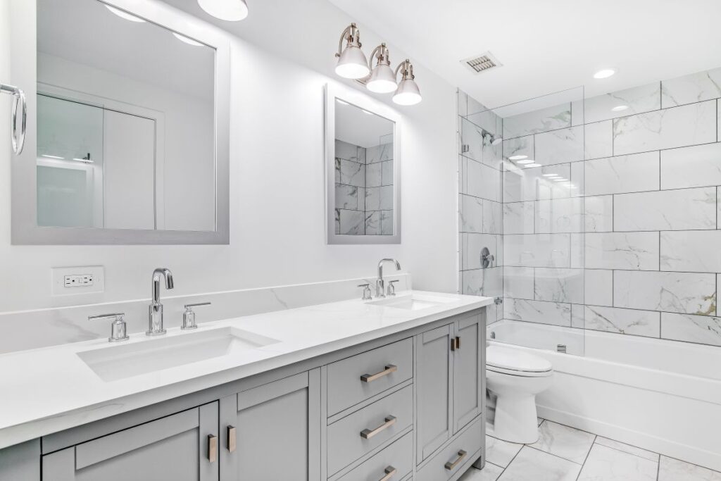 Bright white bathroom with double vanity, quartz countertop and marble tile walls.