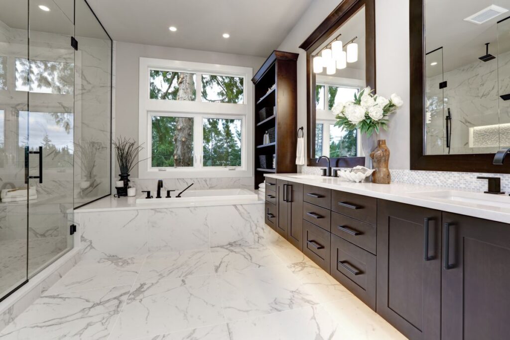 Luxurious bathroom with dark wood vanity, marble floors and walls, glass shower enclosure and soaking tub.