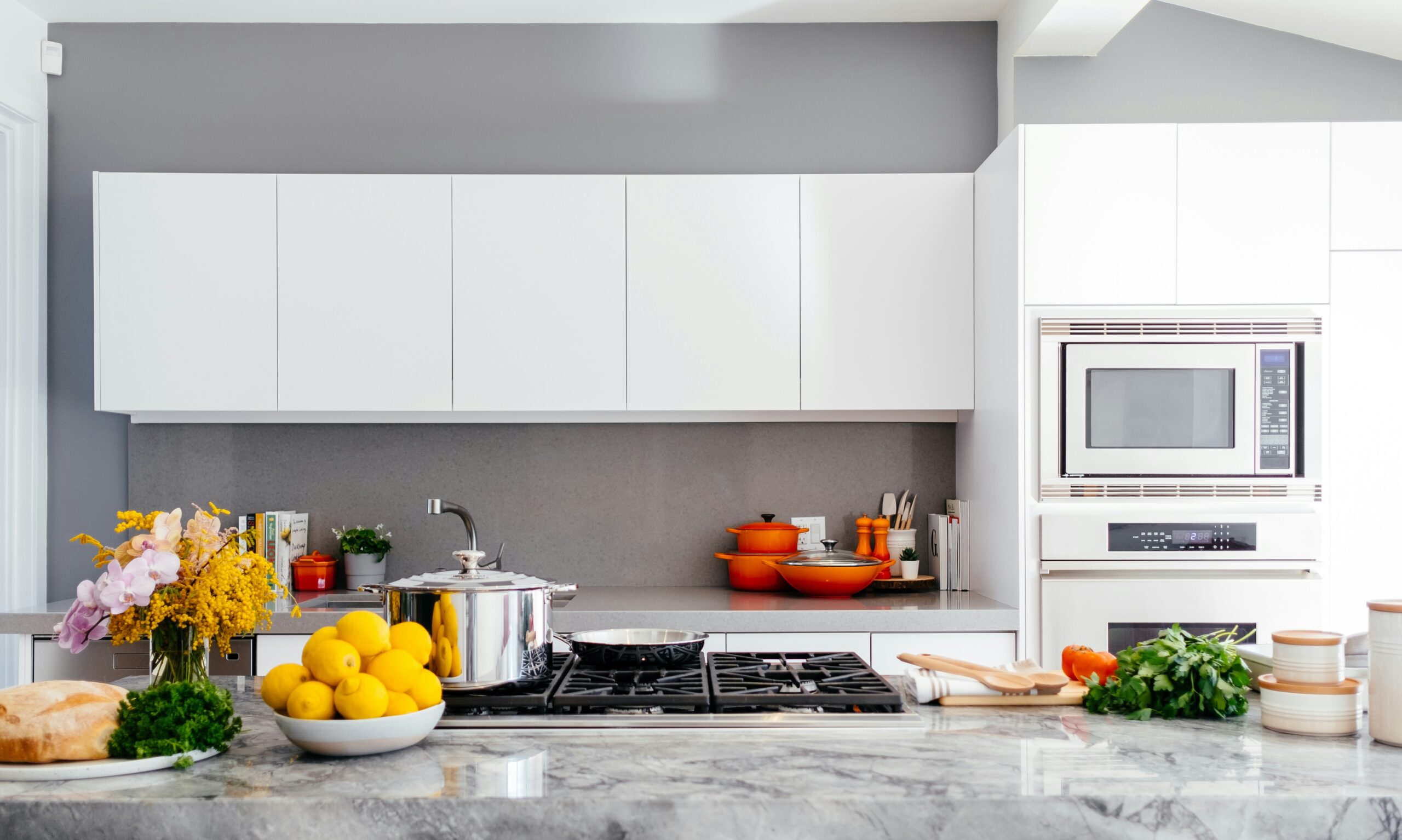 Modern kitchen with white cabinets and a stone island countertop with built in cooktop and fresh produce