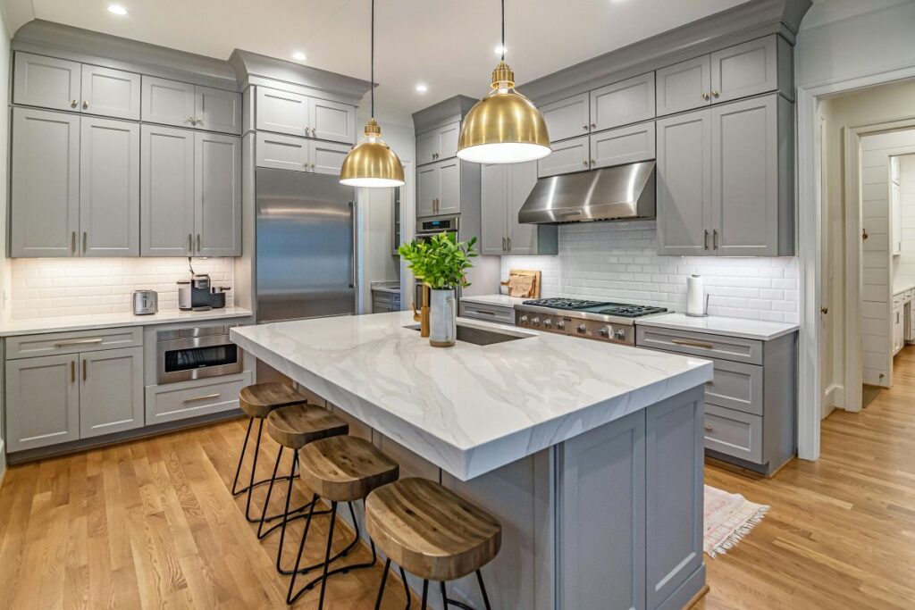 Spacious gray kitchen with marble island, wood stools, and gold pendant lighting.