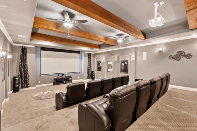at-home movie theater in basement with projector, tiered seating and wooden beams in ceiling