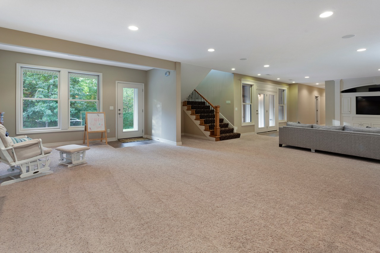 finished lower level basement with large windows, staircase and entertainment area