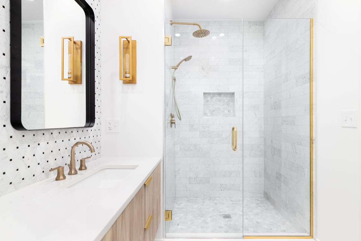 Modern bathroom with a glass walk in shower, floating vanity, marble tile, and brushed brass fixtures.