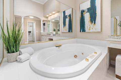 Master bathroom with a large soaking tub, oversized mirror, and modern gold accents.