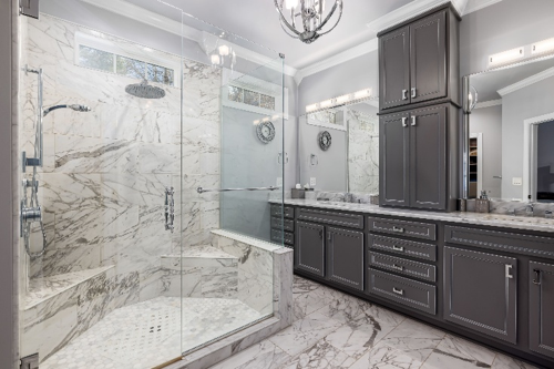 Luxury master bathroom with a marble walk in shower, double vanity, and dark custom cabinetry.