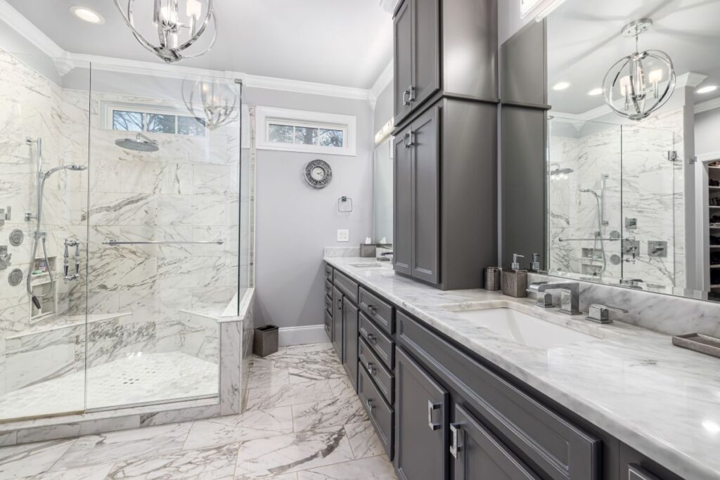 Custom bathroom vanity with full height storage cabinets, marble countertops, and a spacious walk in shower.