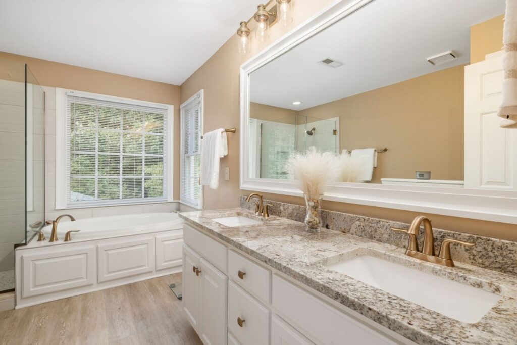 Bathroom remodeling project featuring a white double vanity, granite countertops, walk in glass shower, soaking tub, and modern fixtures.